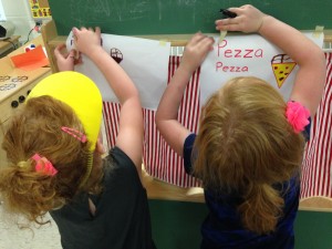 Social/Emotional, Literacy/Fine Motor: Hanging up their signs for the "Pizza Pizza" store